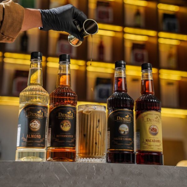 Gelas latte dengan sentuhan Denali Almond Syrup di barista station