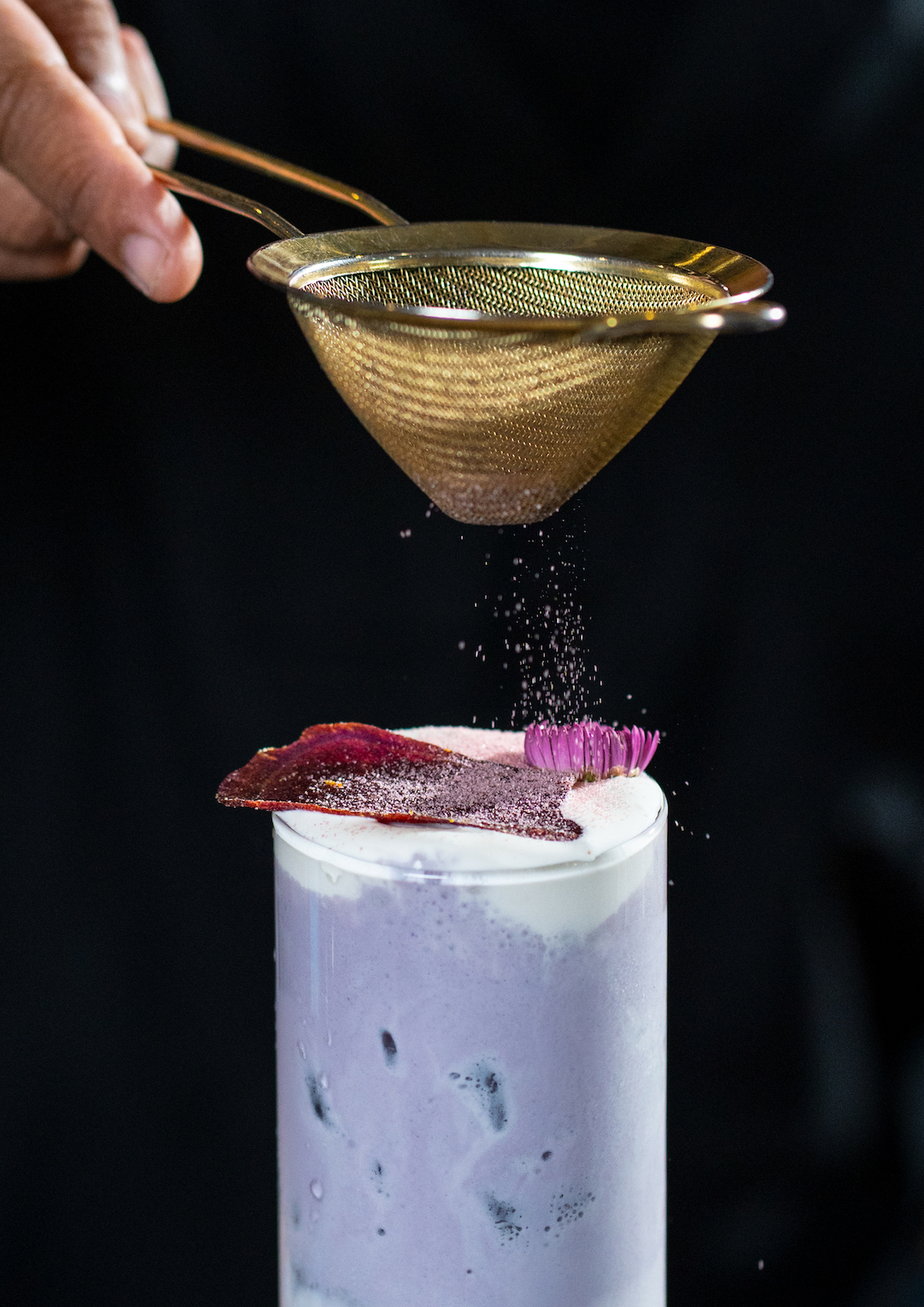 Sunny Taro Cloud dengan Denali Taro Powder, fresh milk, whipping cream, keripik ubi, dusting ubi, dan edible flower dalam High Ball Glass.