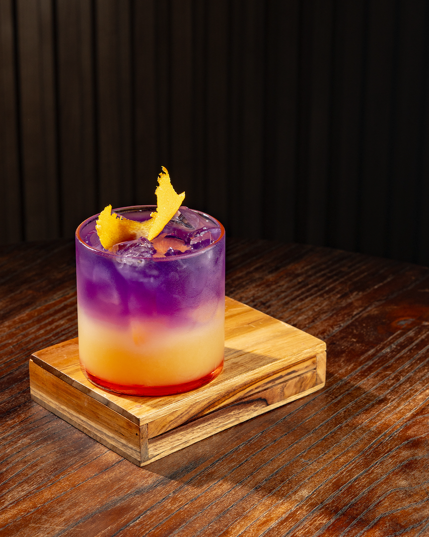 Purple Teeth, mocktail layering citrus gradasi warna jingga ungu dengan garnish orange peel di Old Fashioned glass
